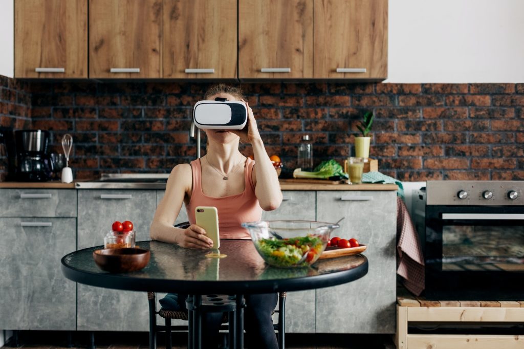 Athletic young woman in a virtual reality headset at home in her kitchen orders food, smart home