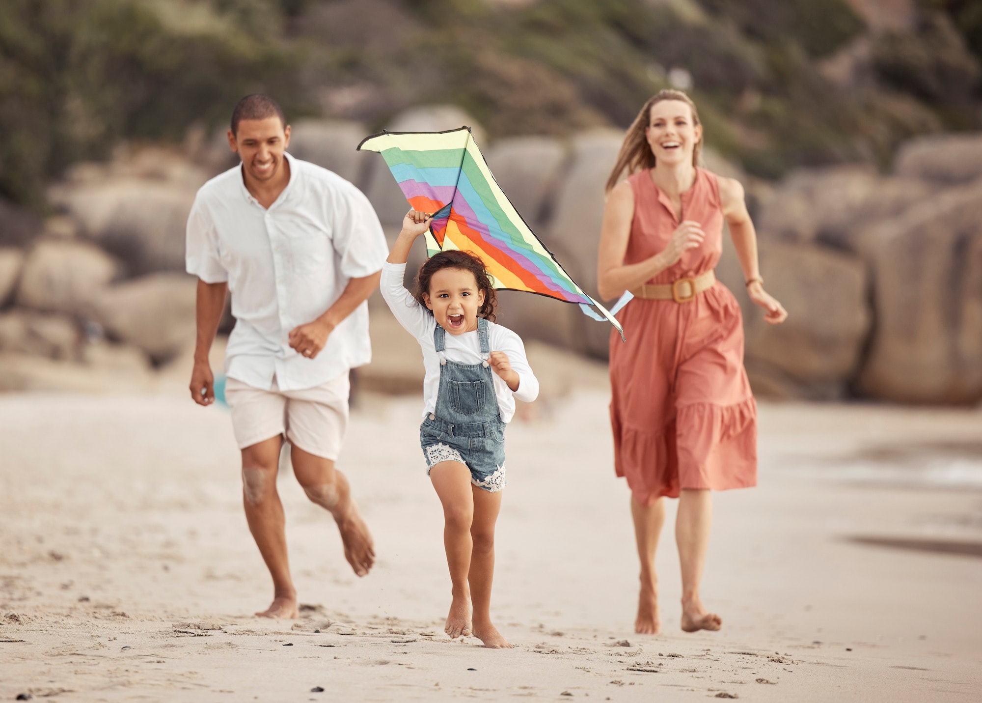 Happy family with child and a kite on the beach in summer for wellness, growth and energy while run